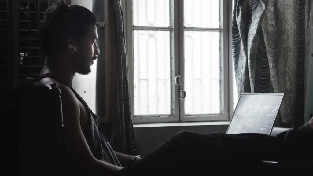 Parent reading on a laptop beside a sunny window with sheer curtains